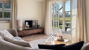 A living room with a sofa, a TV, a wooden cabinet, and a table with a magazine. - Villa With Expansive Sunny Garden (Egmond aan den Hoef)