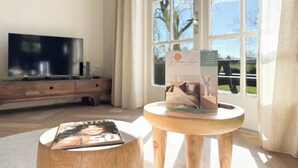 A room with a wooden TV stand, a magazine on a stool, and a window with curtains. - Villa With Expansive Sunny Garden (Egmond aan den Hoef)