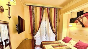 A hotel room with a bed, a desk, a chair, a television, and a window with curtains. - Double with Terrace (Roma)