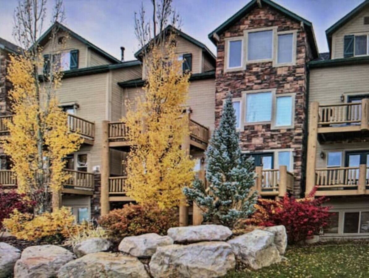 A multi-story building with balconies, surrounded by autumn foliage and rocks.