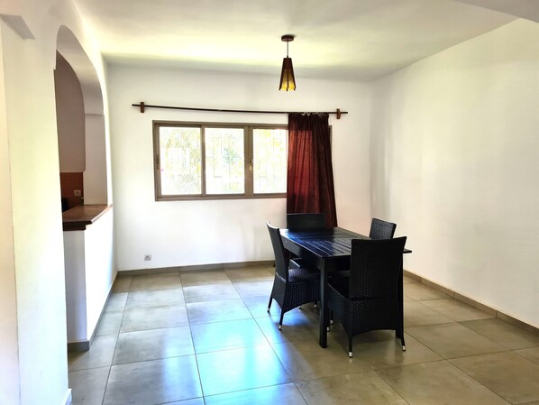 A room with a dining table and chairs, a window with curtains, and a hanging light fixture.