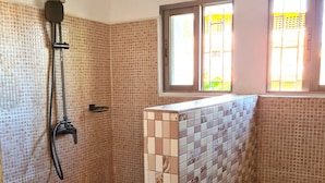Une salle de bain avec une douche, des murs carrelés, une fenêtre et des toilettes.
