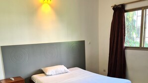 Un lit bien fait, avec une tête de lit, une table de chevet avec une lampe et une fenêtre avec des rideaux.
