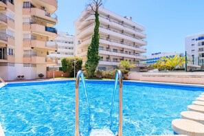 A swimming pool with metal ladders, surrounded by multi-story buildings with balconies and a clear sky. - S102-011 UHC MURILLO APARTMENT (Salou)