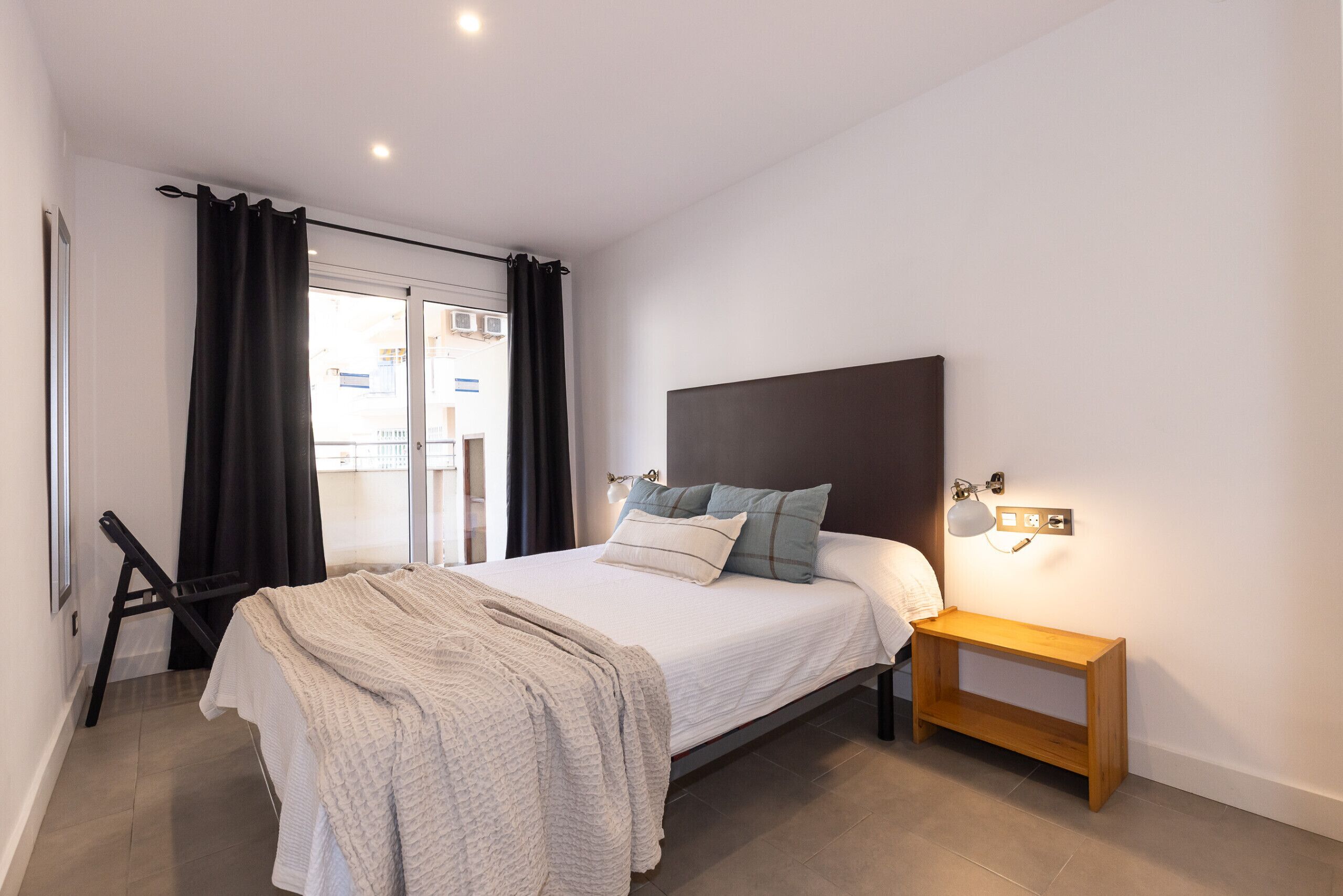 Une chambre à coucher avec un lit, une table de chevet, une fenêtre avec des rideaux et une vue sur l’extérieur.