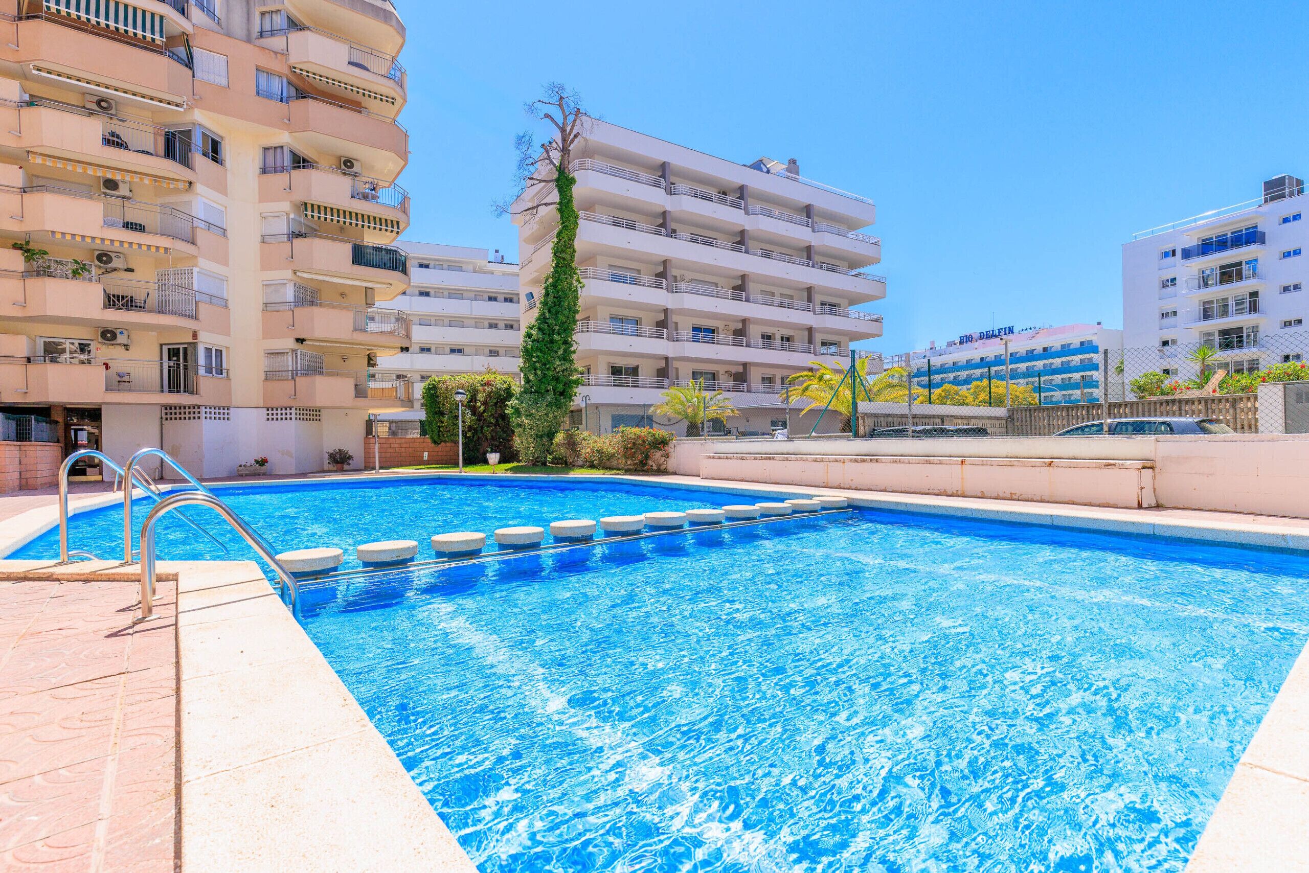 A swimming pool with a clear blue water, surrounded by multi-story buildings with balconies.