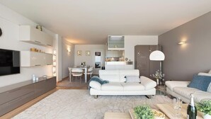 Ein modernes Wohnzimmer mit Sofa, Couchtisch und Fernseher. Es gibt einen Essbereich mit Tisch und Stühlen.