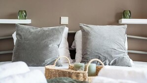 Ein Bett mit grauen Kissen, einem weißen Kopfteil und einem Nachttisch mit einer grünen Vase und Kerzen.