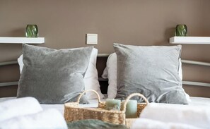 Ein Bett mit grauen Kissen, einem weißen Kopfteil und einem Nachttisch mit einer grünen Vase und Kerzen.