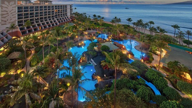 Ein Resort mit mehreren Pools, Palmen und Blick auf den Ozean.