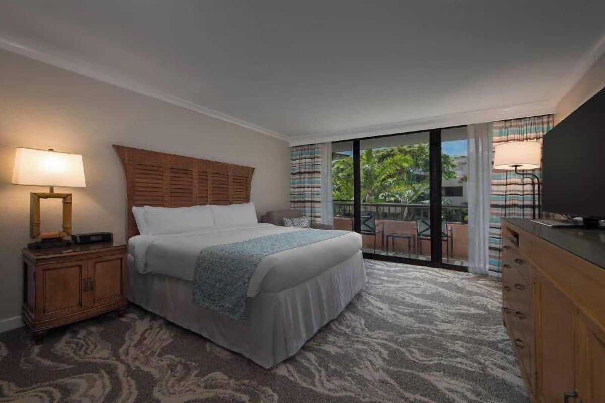 Ein Hotelzimmer mit Bett, Fernseher, Lampe, Holzschrank und einem Balkon mit Blick.