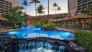 Ein Hotelpoolbereich mit Wasserfall, Palmen und Liegestühlen.