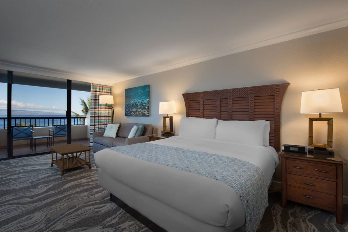Ein Hotelzimmer mit einem großen Bett, einem Balkon mit Blick, einem Schreibtisch und einem Sessel.