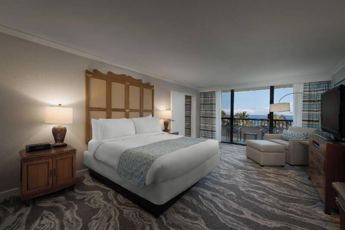 Ein Hotelzimmer mit einem großen Bett, einem Sofa, einem Fernseher und einem Balkon mit Blick.