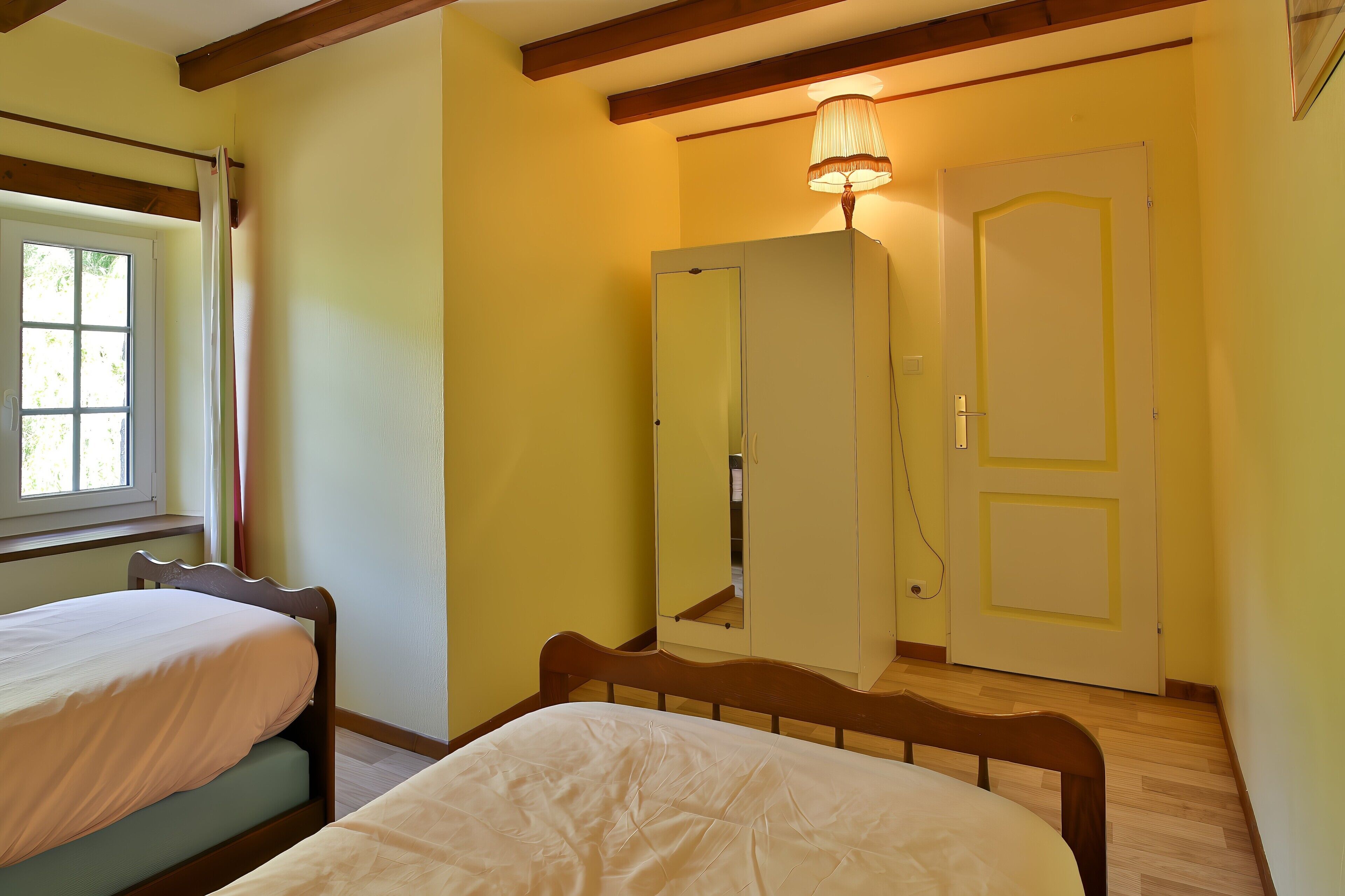 A bedroom with two beds, a wardrobe, a mirror, and a window.