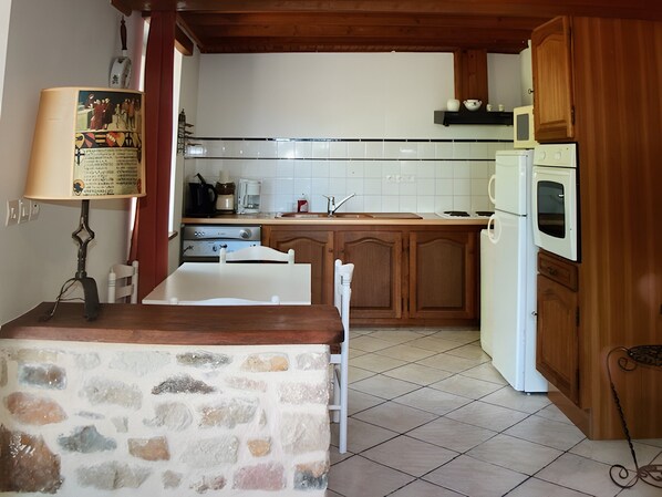 A kitchen with a stone countertop, wooden cabinets, a white refrigerator, and a microwave.