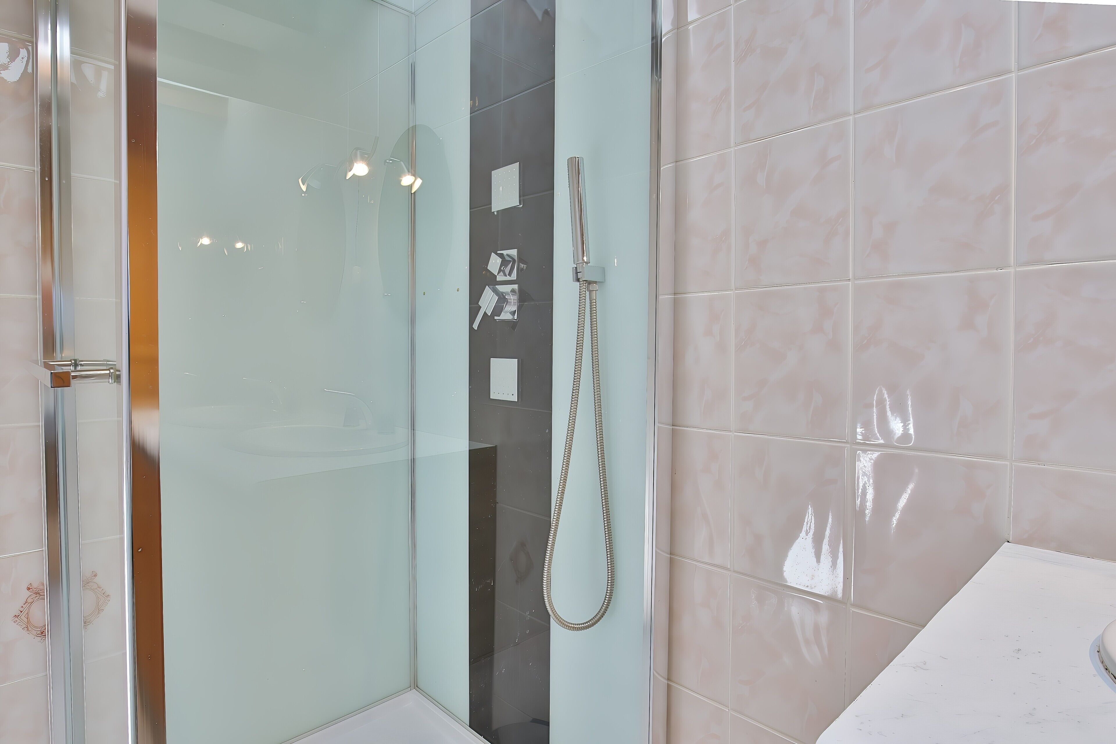 Een moderne badkamer met een glazen douchecabine, een handdouche en een wand betegeld met marmer.