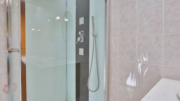 Een moderne badkamer met een glazen douchecabine, een handdouche en een wand betegeld met marmer.