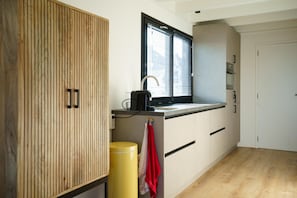 A compact kitchen with wooden cabinetry, a window with blinds, and a yellow trash bin. - Stylish Boathouse on Lake Sneeker (Offingawier)