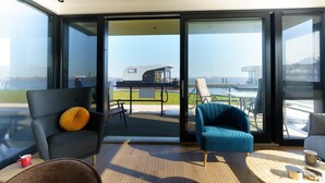 A modern interior with a large sliding glass door leading to a deck with a view of a boat and water. - Stylish Boathouse on Lake Sneeker (Offingawier)