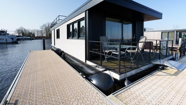 A modern floating houseboat with a covered deck, a small outdoor seating area, and a glass-enclosed room. - Stylish Boathouse on Lake Sneeker (Offingawier)