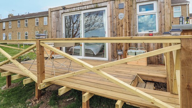 Um deck de madeira com vista para uma casa com grandes janelas e uma varanda.