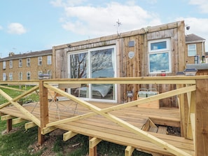 Une terrasse en bois offrant une vue sur une maison dotée de grandes fenêtres et d’un balcon.