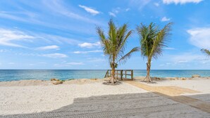 A beach with two palm trees, a wooden deck, and a sandy shoreline. - Fully Remodeled First-Floor Condo | Steps to Beach | Siesta Key (Sarasota)