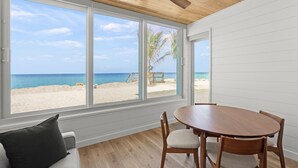 A room with a wooden ceiling, large windows with a beach view, a round wooden table, and a gray sofa. - Fully Remodeled First-Floor Condo | Steps to Beach | Siesta Key (Sarasota)