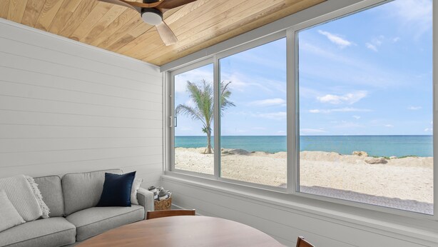 A room with a large window, a wooden ceiling fan, a gray sofa, and a wooden dining table. - Fully Remodeled First-Floor Condo | Steps to Beach | Siesta Key (Sarasota)