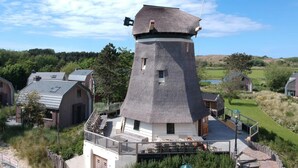 Un molino de viento con balcón, rodeado de edificios y follaje.
