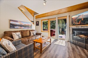 A cozy living room with a fireplace, a sofa, a coffee table, and a painting of a mountain landscape. - Fall River Hideout • Private Hot Tub • Near RMNP (Estes Park)