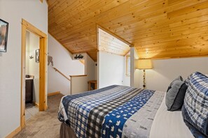 Et soveværelse med træloft, en seng med et ternet tæppe, et natbord og en lampe.