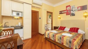 A hotel room with a bed, a small kitchenette, a dining table, and a bathroom visible through an open door. - Superior Double with Terrace (Roma)