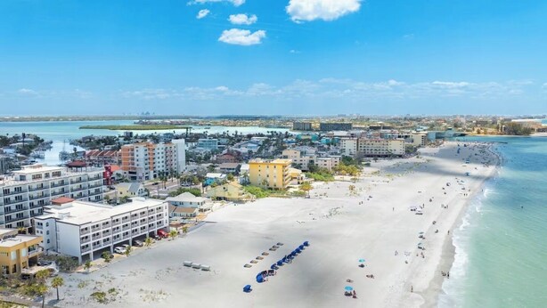 Un paysage urbain côtier avec une vaste plage de sable, des bâtiments situés en bord de mer et un ciel dégagé.