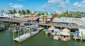 A waterfront area with docked boats, a wooden pier, and buildings with thatched-roof structures. - Amazing Newer Condo in Madeira Beach just steps from the Ocean and John's Pass! (Madeira Beach)