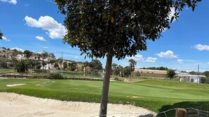 Ein Golfplatz mit blauem Himmel, einem Verbotsschild und einem Baum im Vordergrund.