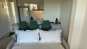 Ein Hotelzimmer mit einem großen Bett, einem kleinen Schreibtisch mit Stuhl, einer Küchenzeile und einem Badezimmer.