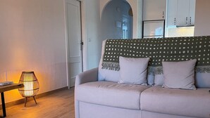 Ein Wohnzimmer mit einer Couch, einer Lampe, einem Deckenventilator und einer Küche im Hintergrund.