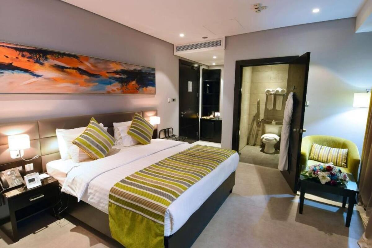 Una habitación de hotel con cama, mesita de noche, lámpara y un cuadro en la pared.