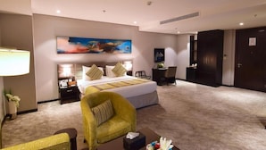 A hotel room with a bed, a desk, a chair, a lamp, and a painting on the wall. - Best Plus Aurora Hotel (Riyadh)