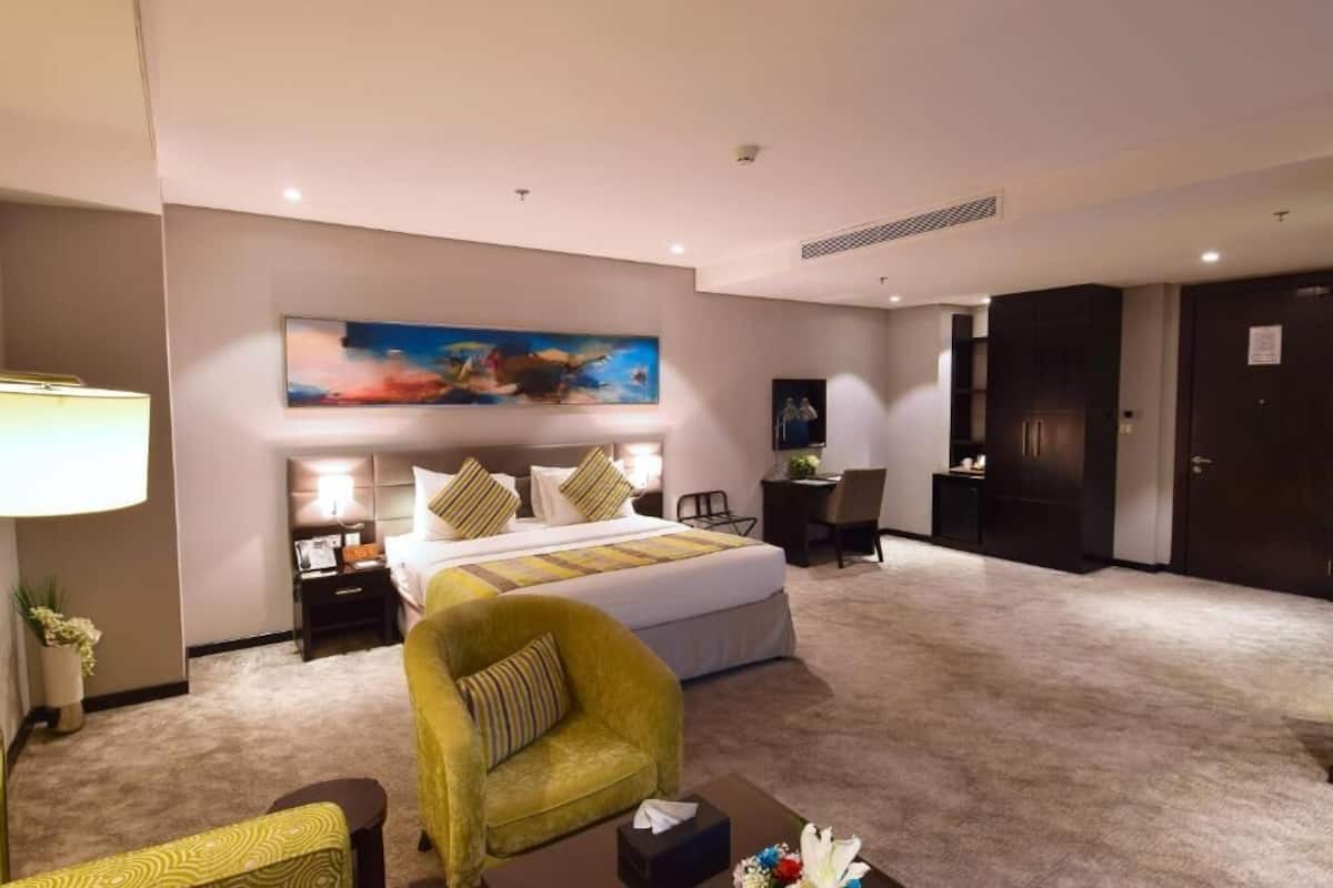 Habitación de hotel con cama, escritorio, silla, lámpara y un cuadro en la pared.