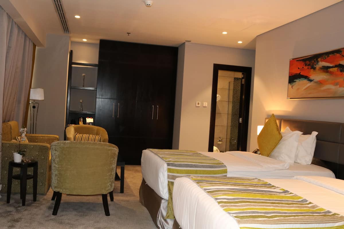 Habitación de hotel con dos camas, una zona de estar con sillas, un escritorio y un cuadro grande en la pared.