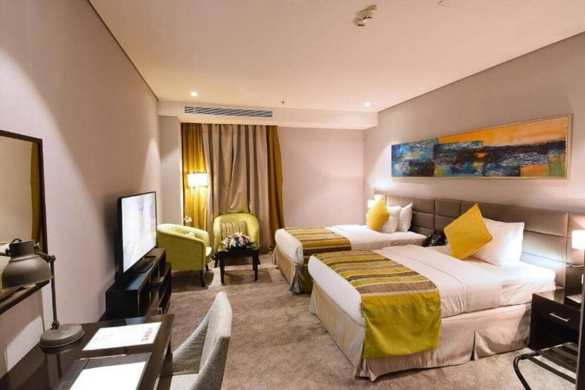 Habitación de hotel con dos camas, televisión, escritorio, silla y un cuadro en la pared.