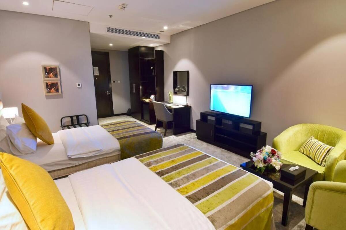 Habitación de hotel con dos camas, un escritorio, un televisor y un sillón verde.