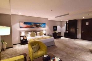 A hotel room with a large bed, a desk, a chair, and a painting on the wall. - Best Plus Aurora Hotel (Riyadh)