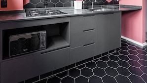 A modern kitchen with a pink wall, black hexagonal tiles, a wooden shelf with glasses, and a built-in stove. - ZEST Cardeal (São Paulo)