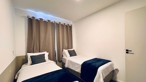 A small, clean room with two beds, a curtain, a door, and a ceiling light. - ZEST Cardeal (São Paulo)