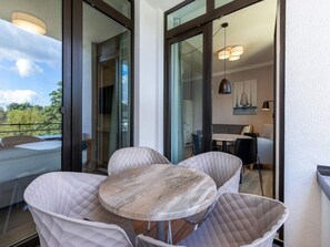 Ein Balkon mit Tisch und Stühlen, eine Schiebetür zu einem Essbereich und Blick ins Grüne.
