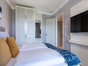 Ein Schlafzimmer mit einem Bett, Kissen, einem Kleiderschrank, einem Fernseher und einer Tür zu einem anderen Raum.